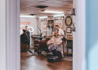 Professional barbers cutting hair of male clients sitting on chairs in traditional barbershop
