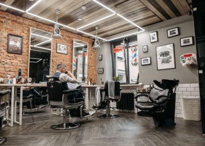 A sleek and stylish barbershop interior featuring upholstered chairs, mirrors, and customers.