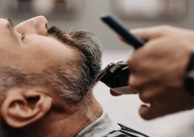 Close-up of a barber using clippers to groom a client's beard in a barbershop.